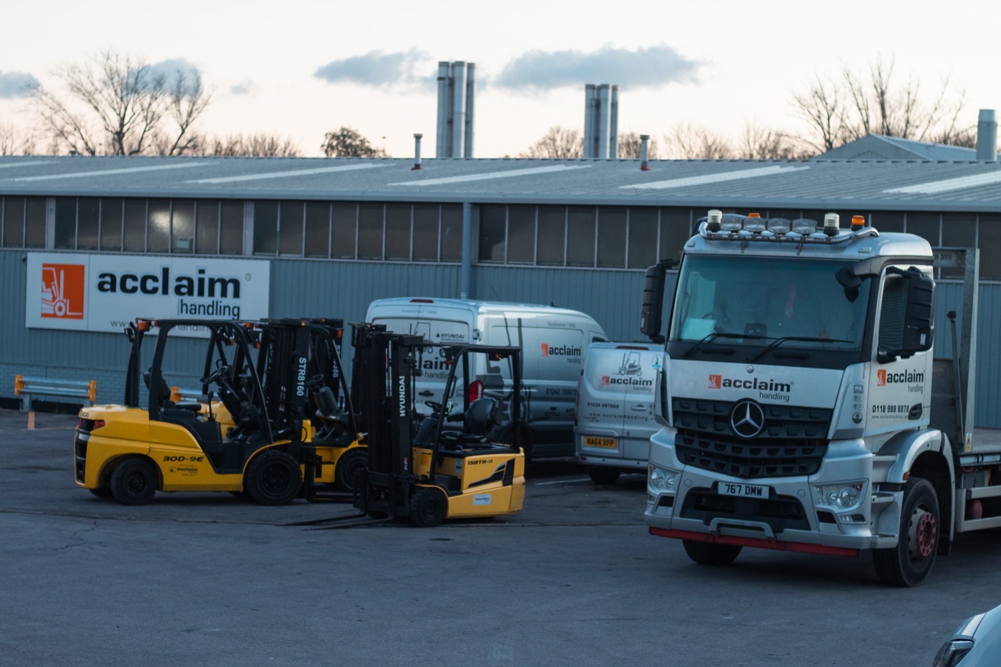 Acclaim hire forklifts lined up in a depot yard beside an Acclaim lorry