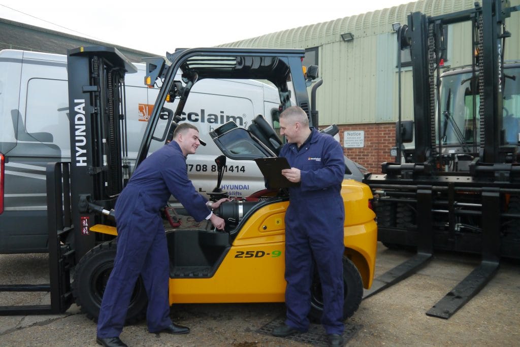 Two Acclaim Handling engineers in branded overalls repairing a Hyundai counterbalance forklift beside an Acclaim service van