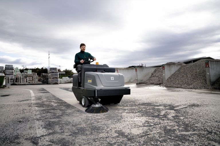 A ride-on industrial sweeper at work in a yard
