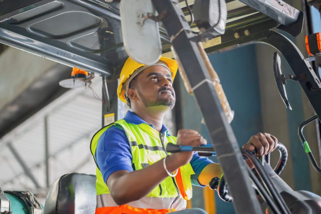 forklift driver in a warehouse wearing a yellow safety helmet