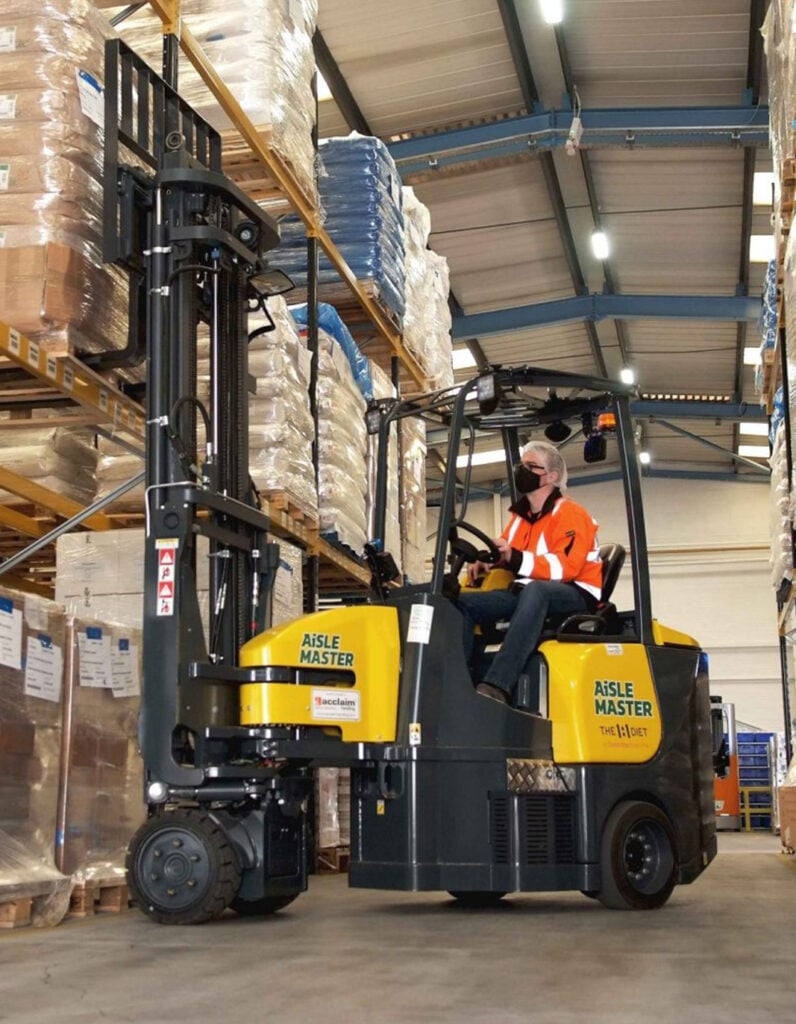 Operator driving an articulated forklift down a narrow racking aisle