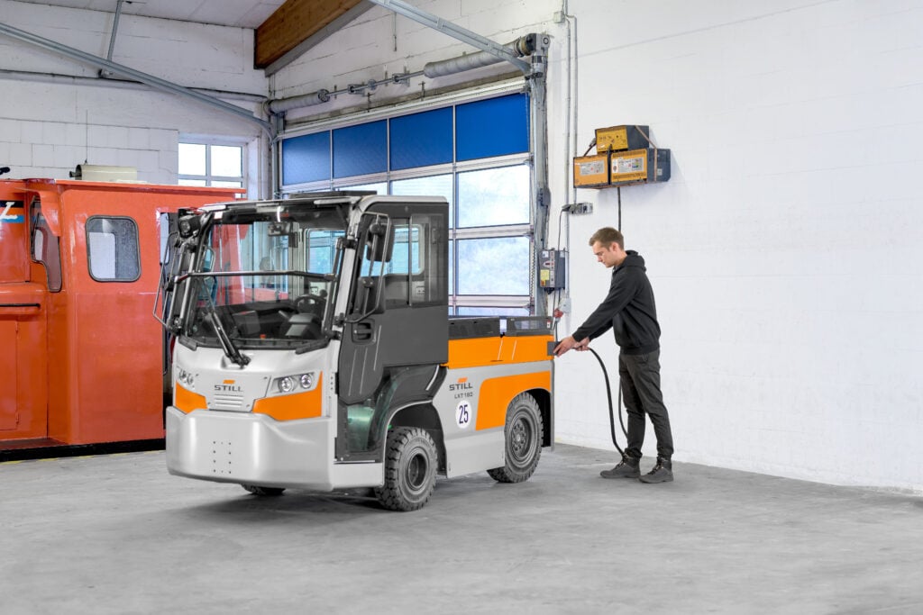 Warehouse truck connected to its battery charger in a charging area